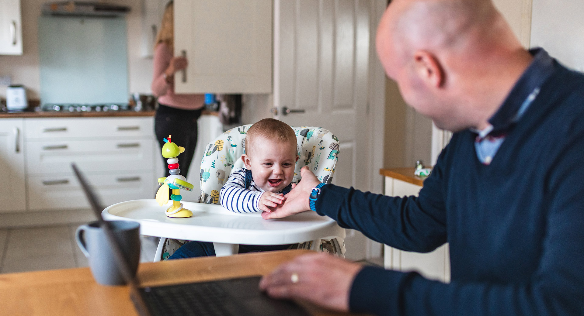 A person playing with a baby in a highchair
                        