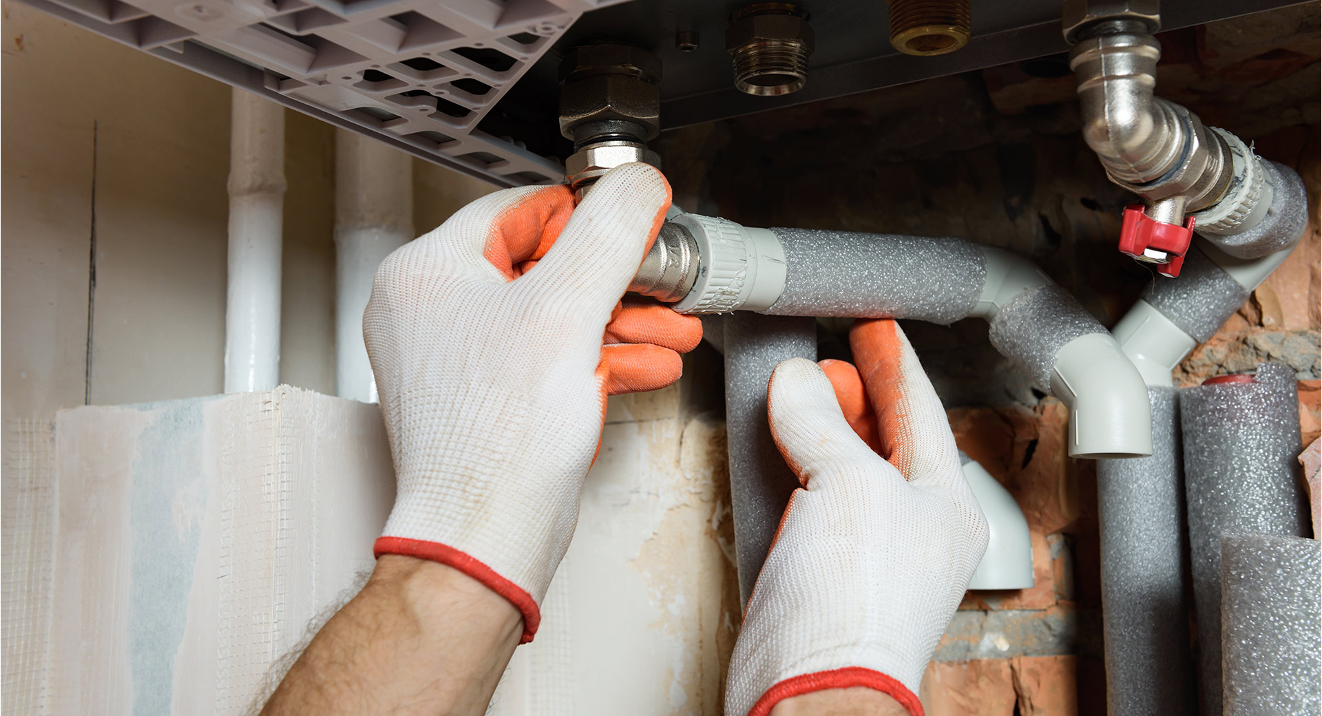 A worker fixing pipes with gloves on
                        