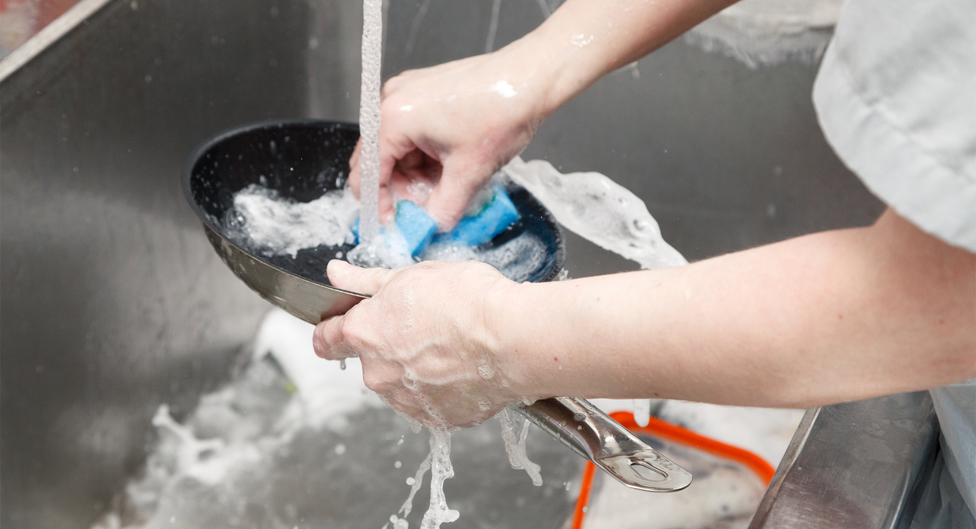 A person washing a pan in a sink
                        